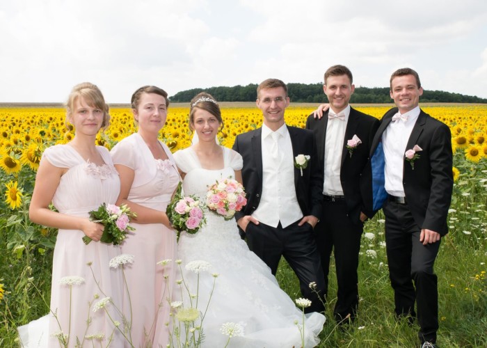 brautpaar mit trauzeugen vor einem feld sonnenblumen